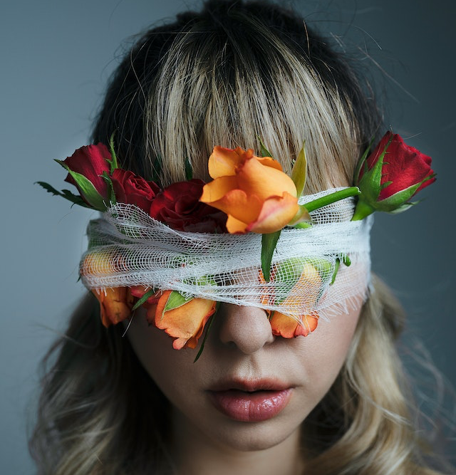 Eine blonde Frau mit verbundenen Augen und Blumen hinter der Binde